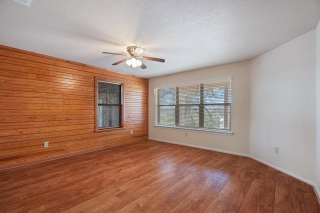 spare room featuring a textured ceiling, hardwood / wood-style flooring, ceiling fan, and wooden walls