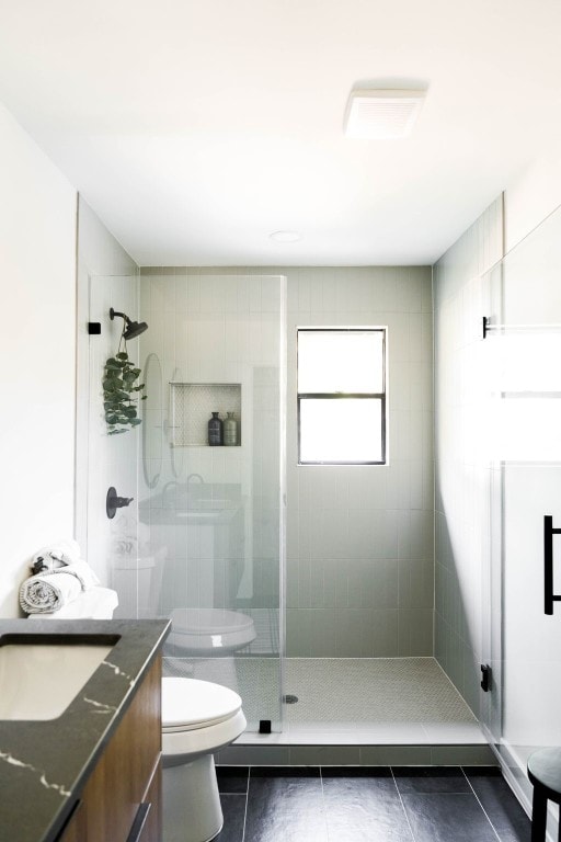 bathroom featuring tile patterned flooring, toilet, a tile shower, and vanity