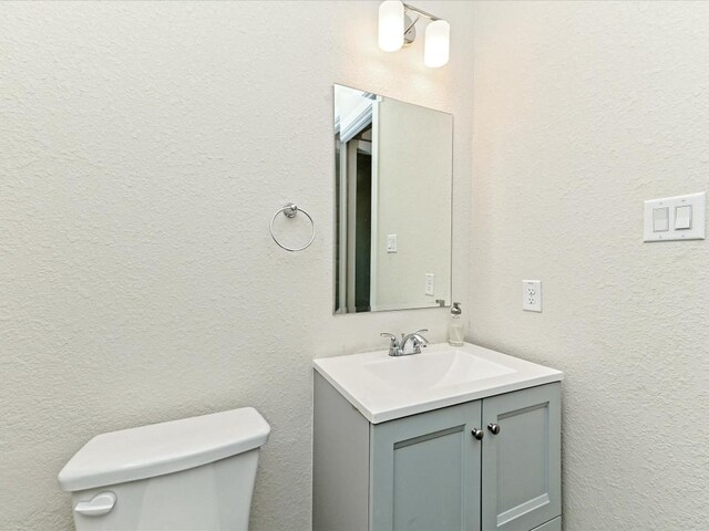 bathroom with a textured wall, vanity, and toilet