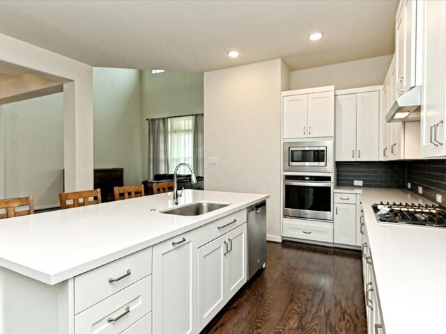 kitchen featuring a center island with sink, appliances with stainless steel finishes, dark wood-style flooring, under cabinet range hood, and a sink