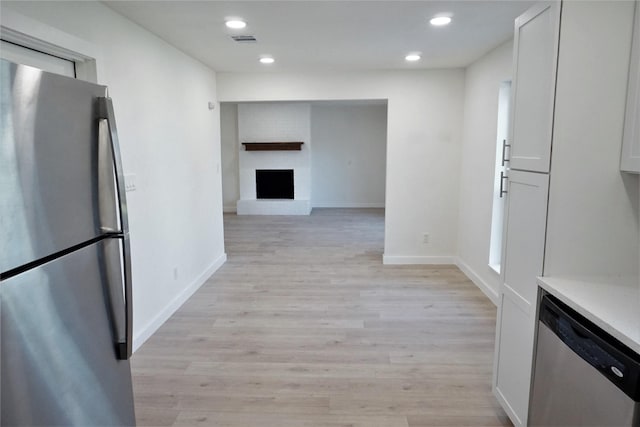 kitchen featuring white cabinetry, stainless steel appliances, a brick fireplace, and light hardwood / wood-style flooring