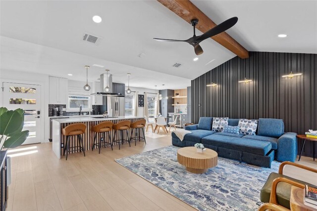 living room with vaulted ceiling with beams, ceiling fan, light hardwood / wood-style floors, and sink