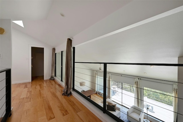 corridor with light wood-type flooring and lofted ceiling with skylight