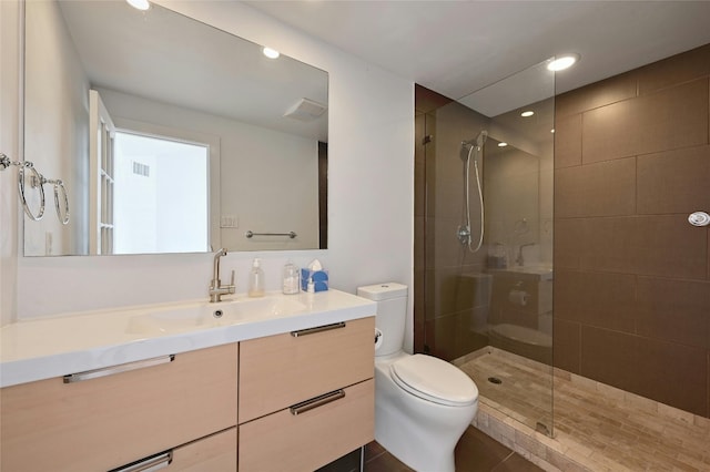 bathroom featuring tile patterned flooring, a tile shower, vanity, and toilet