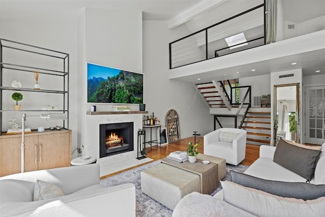 living room with light hardwood / wood-style floors, a premium fireplace, beam ceiling, and high vaulted ceiling