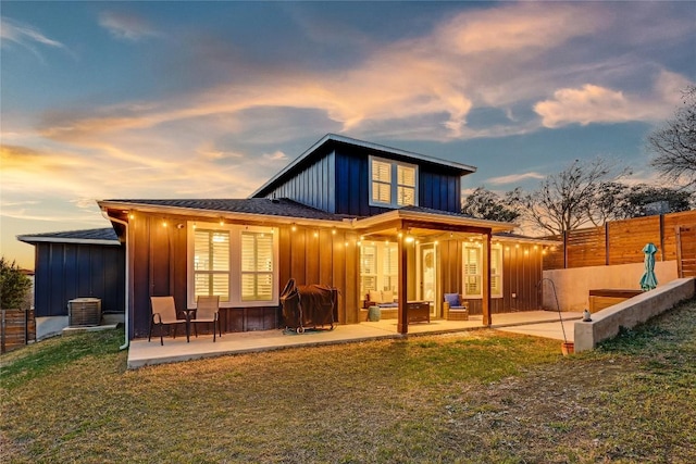 back of property at dusk featuring a patio, a lawn, central AC unit, board and batten siding, and fence