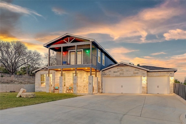 view of front of house featuring an attached garage, a balcony, fence, stone siding, and driveway