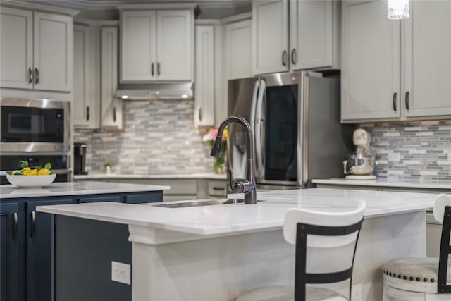 kitchen with decorative backsplash, appliances with stainless steel finishes, a breakfast bar area, light countertops, and under cabinet range hood