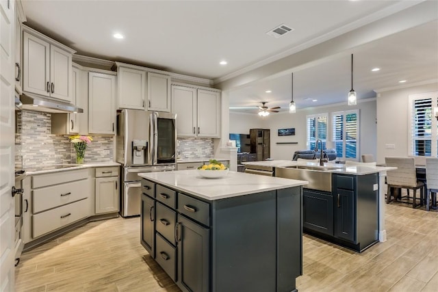 kitchen with stainless steel refrigerator with ice dispenser, ornamental molding, a kitchen island, a sink, and under cabinet range hood