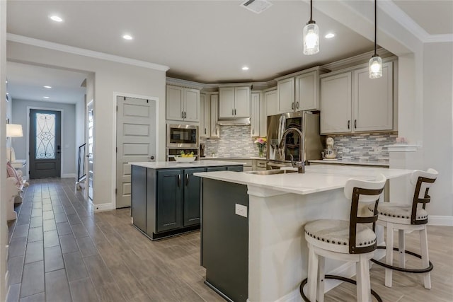 kitchen featuring crown molding, stainless steel appliances, visible vents, a kitchen island with sink, and a sink