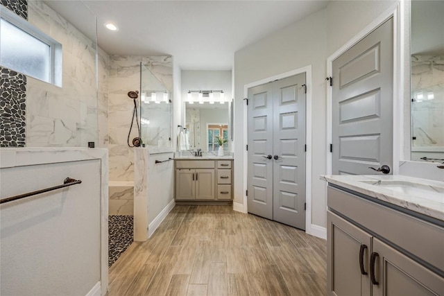 bathroom with wood finish floors, two vanities, a sink, and a marble finish shower