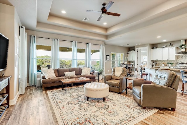 living room with light hardwood / wood-style floors, a raised ceiling, and ceiling fan