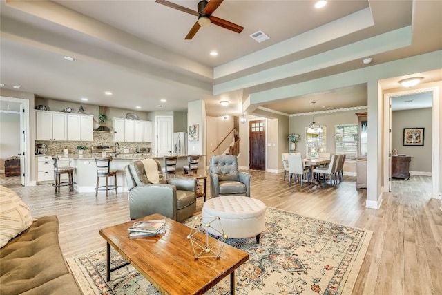 living room featuring light hardwood / wood-style floors, a raised ceiling, ceiling fan, and sink