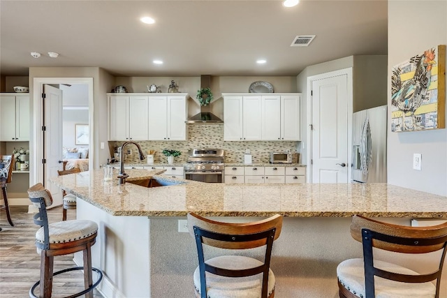 kitchen with wall chimney range hood, sink, appliances with stainless steel finishes, light stone counters, and white cabinetry