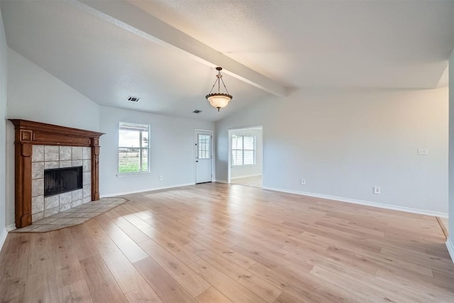 unfurnished living room featuring lofted ceiling with beams, light hardwood / wood-style floors, and a tiled fireplace