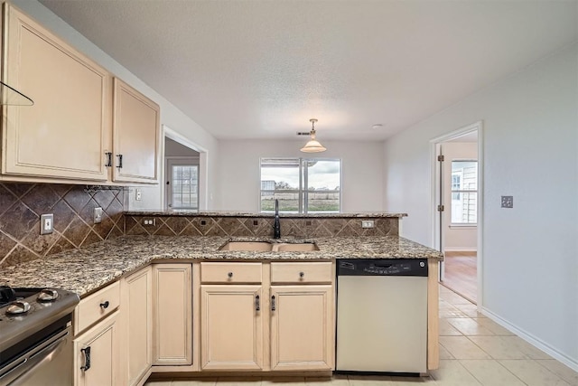 kitchen with dark stone counters, stainless steel appliances, sink, cream cabinetry, and light tile patterned flooring