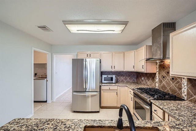 kitchen with dark stone counters, wall chimney exhaust hood, decorative backsplash, light tile patterned floors, and appliances with stainless steel finishes