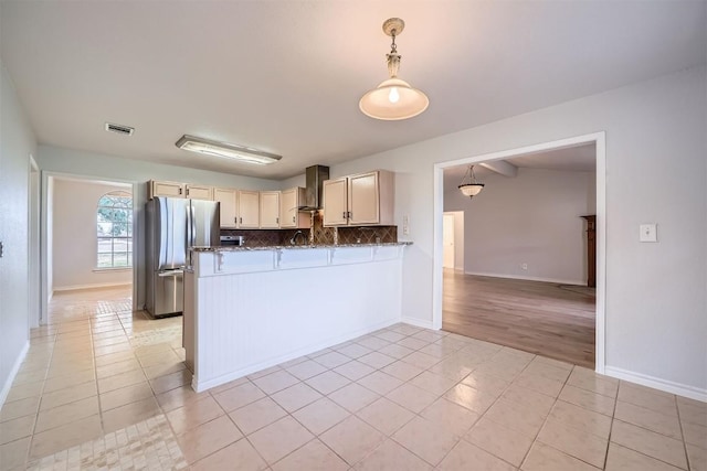 kitchen with kitchen peninsula, stainless steel fridge, tasteful backsplash, wall chimney exhaust hood, and light tile patterned flooring