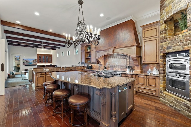 kitchen featuring beam ceiling, light stone countertops, sink, hanging light fixtures, and a large island with sink