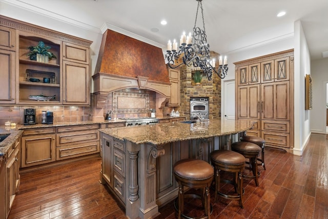 kitchen with sink, hanging light fixtures, backsplash, a center island with sink, and custom exhaust hood