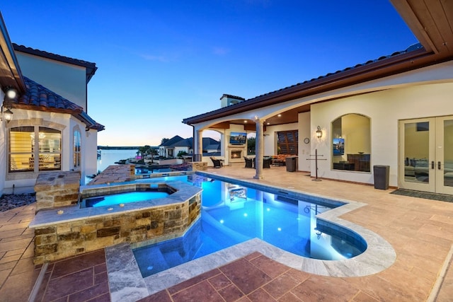 pool at dusk featuring a patio area, a water view, an in ground hot tub, and french doors