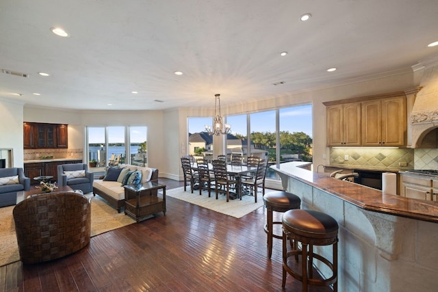 living room with dark wood-type flooring, a water view, a chandelier, and ornamental molding