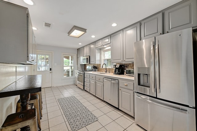 kitchen featuring sink, gray cabinets, light tile patterned floors, tasteful backsplash, and stainless steel appliances