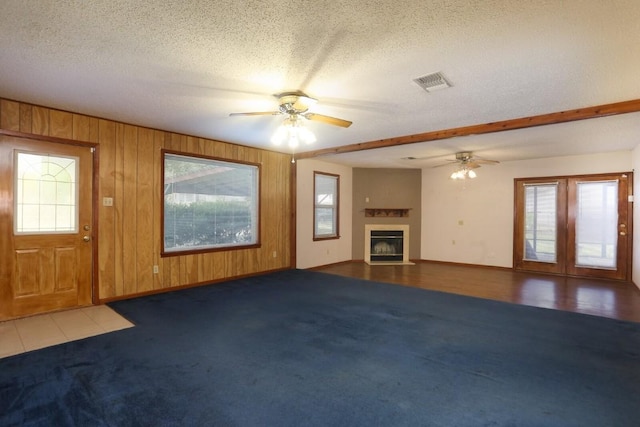 unfurnished living room with wooden walls, plenty of natural light, ceiling fan, and a textured ceiling