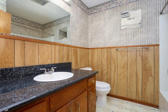 bathroom with vanity, toilet, a textured ceiling, and wooden walls