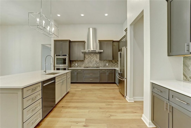 kitchen featuring decorative backsplash, stainless steel appliances, sink, wall chimney range hood, and light hardwood / wood-style flooring