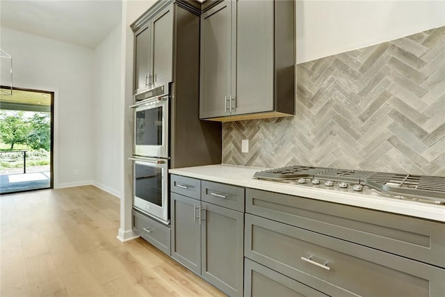 kitchen featuring stainless steel appliances, gray cabinets, tasteful backsplash, and light hardwood / wood-style flooring