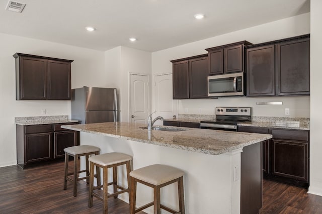 14405 Boomtown Way, Elgin, TX 78621 - kitchen featuring appliances with stainless steel finishes, dark brown cabinets, dark wood-type flooring, a kitchen bar, and recessed lighting