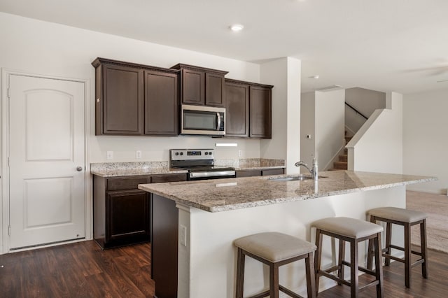 14405 Boomtown Way, Elgin, TX 78621 - kitchen with stainless steel appliances, light stone counters, dark brown cabinets, a breakfast bar area, and dark wood finished floors