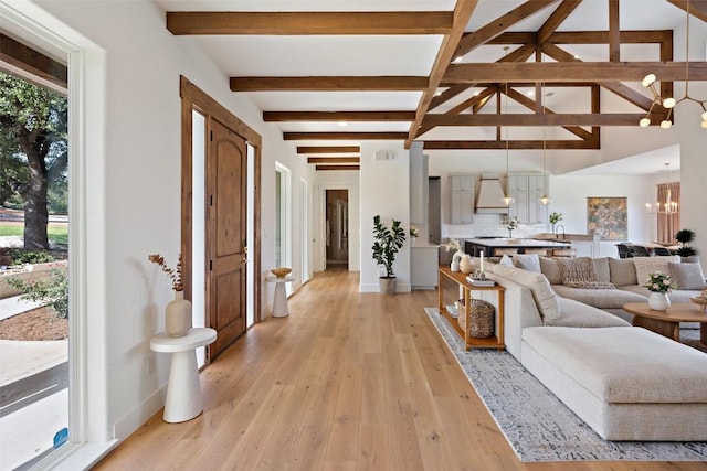 living room featuring vaulted ceiling with beams, plenty of natural light, light hardwood / wood-style floors, and a notable chandelier