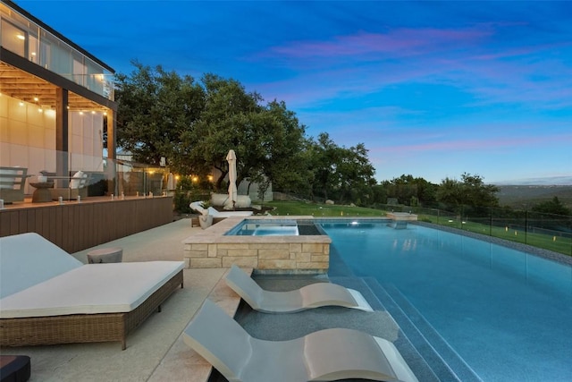 pool at dusk with a patio area and an in ground hot tub