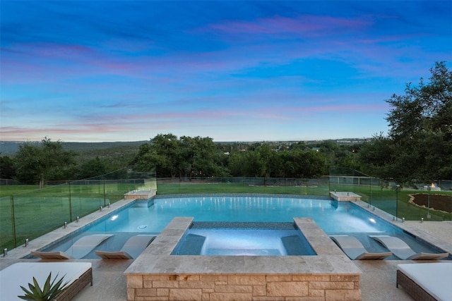 pool at dusk with an in ground hot tub, a yard, and pool water feature