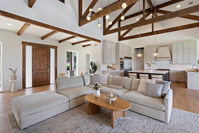 living room featuring beam ceiling, sink, high vaulted ceiling, and light wood-type flooring