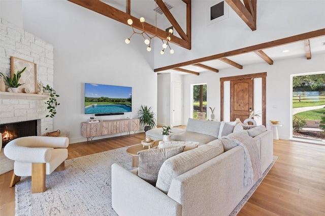 living room featuring beam ceiling, a stone fireplace, and light hardwood / wood-style floors