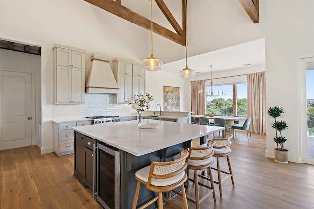 kitchen featuring custom exhaust hood, hanging light fixtures, wine cooler, light stone countertops, and beam ceiling