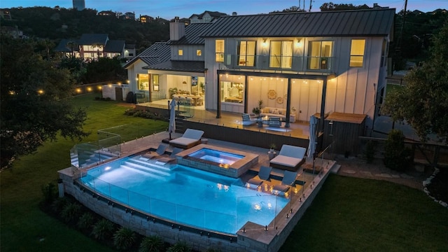 back house at dusk with a lawn, an outdoor living space, a balcony, a patio area, and a swimming pool with hot tub