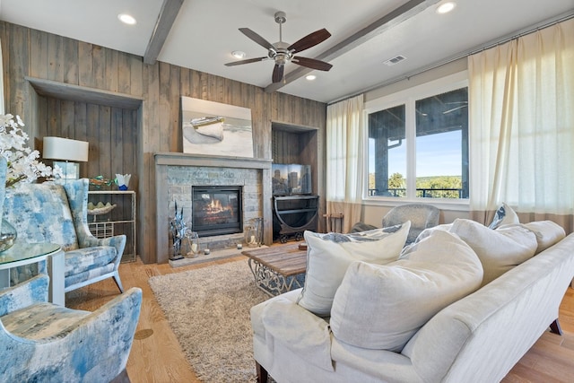 living room with a fireplace, ceiling fan, wooden walls, beamed ceiling, and light hardwood / wood-style floors