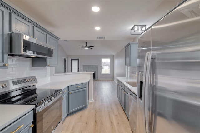 kitchen featuring ceiling fan, light hardwood / wood-style floors, vaulted ceiling, decorative backsplash, and appliances with stainless steel finishes