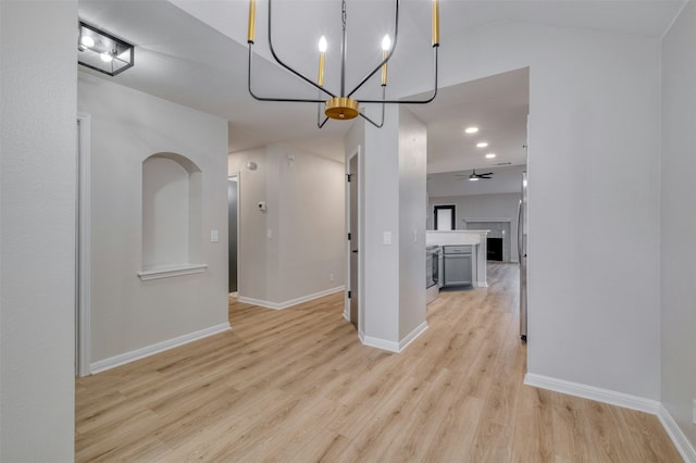 unfurnished dining area featuring ceiling fan with notable chandelier, light wood-type flooring, and lofted ceiling