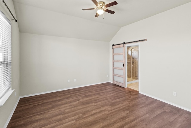 empty room with a barn door, ceiling fan, dark hardwood / wood-style flooring, and lofted ceiling