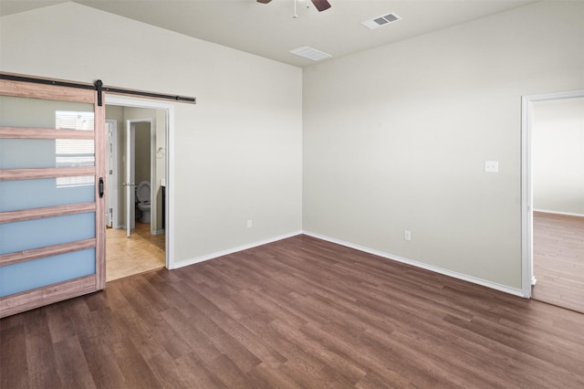 empty room with dark hardwood / wood-style floors, a barn door, and ceiling fan