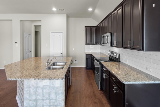 kitchen featuring sink, a kitchen island with sink, light stone counters, decorative backsplash, and appliances with stainless steel finishes