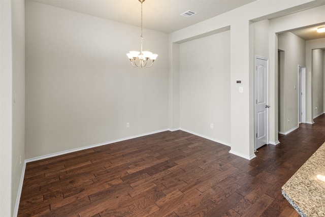 spare room with dark hardwood / wood-style floors and an inviting chandelier