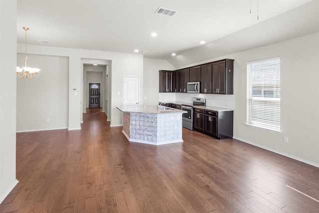 kitchen featuring decorative backsplash, stainless steel appliances, a chandelier, lofted ceiling, and an island with sink