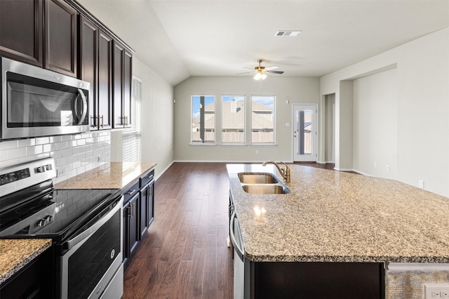 kitchen featuring sink, decorative backsplash, an island with sink, light stone counters, and stainless steel appliances