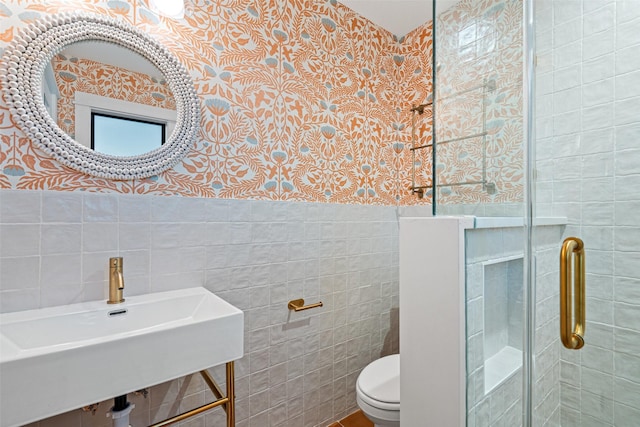 bathroom featuring a shower with shower door, sink, tile walls, and toilet